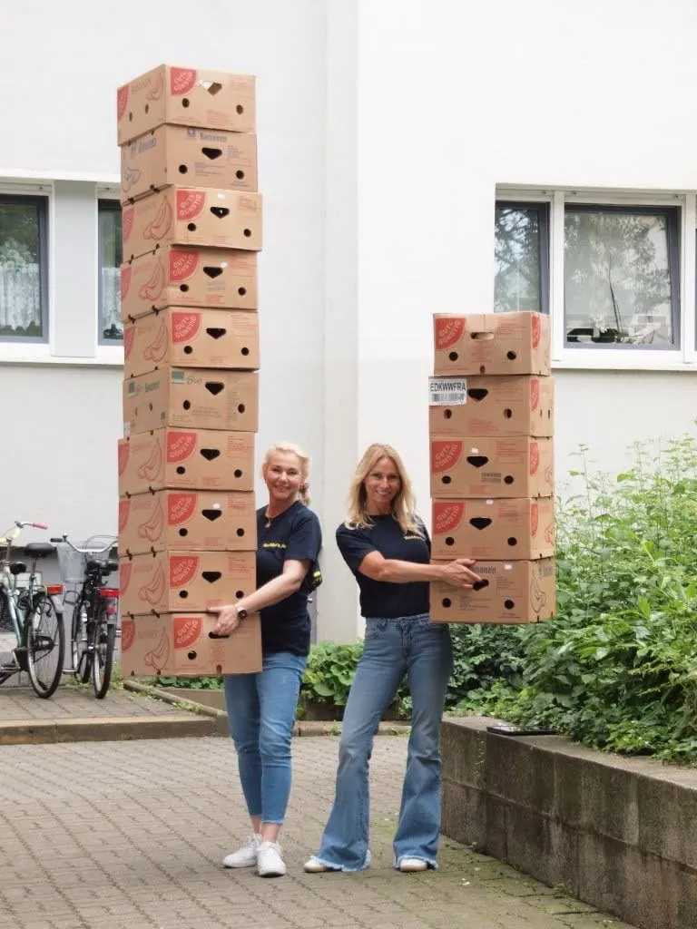 Anette Kochmann und Yvonne Bergmann tragen hohe Stapel Umzugskartons vor einem Haus in Halle (Saale)