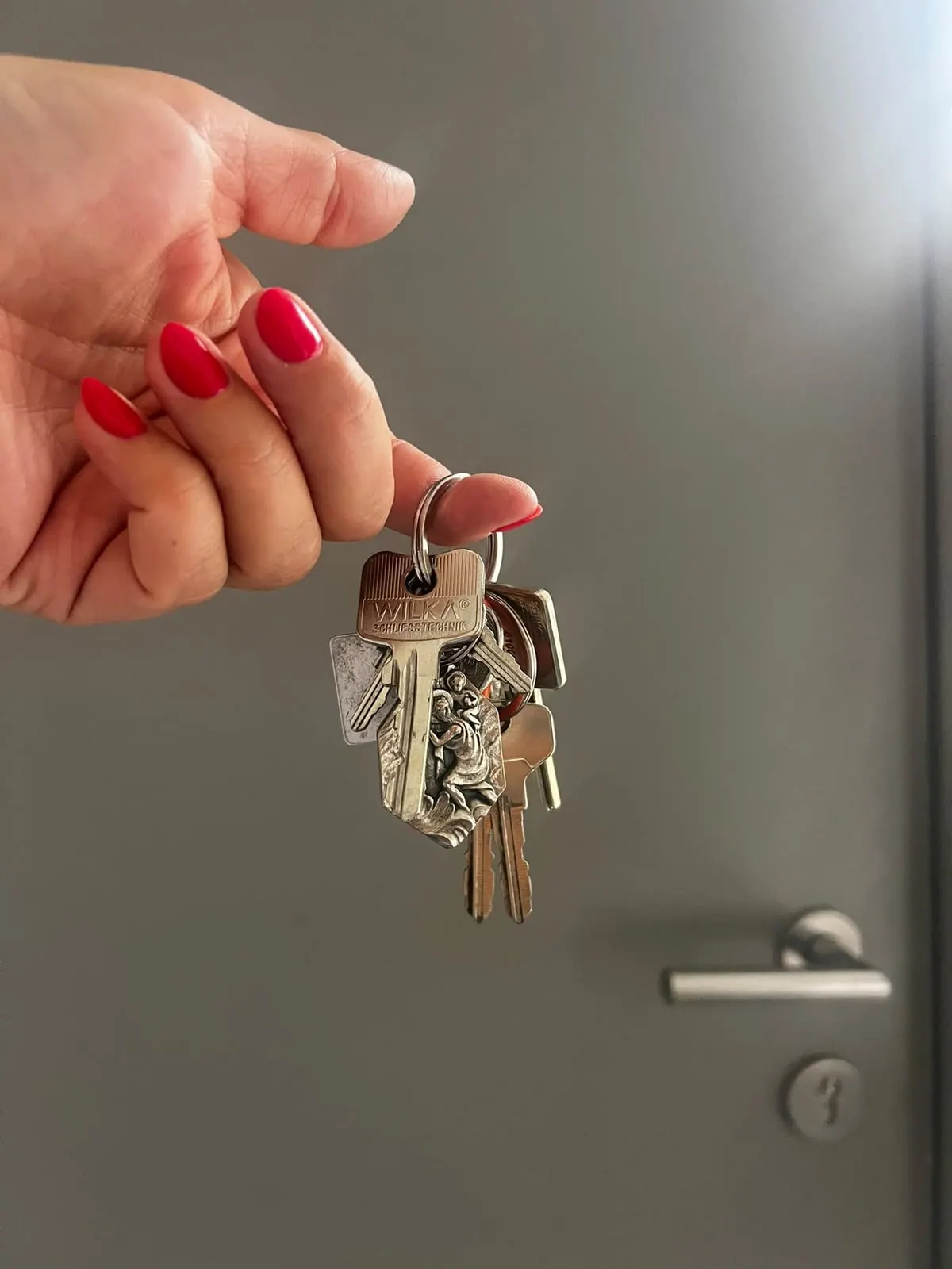 Schlüsselbund mit Wohnungsschlüsseln in der Hand vor einer grauen Wohnungstür