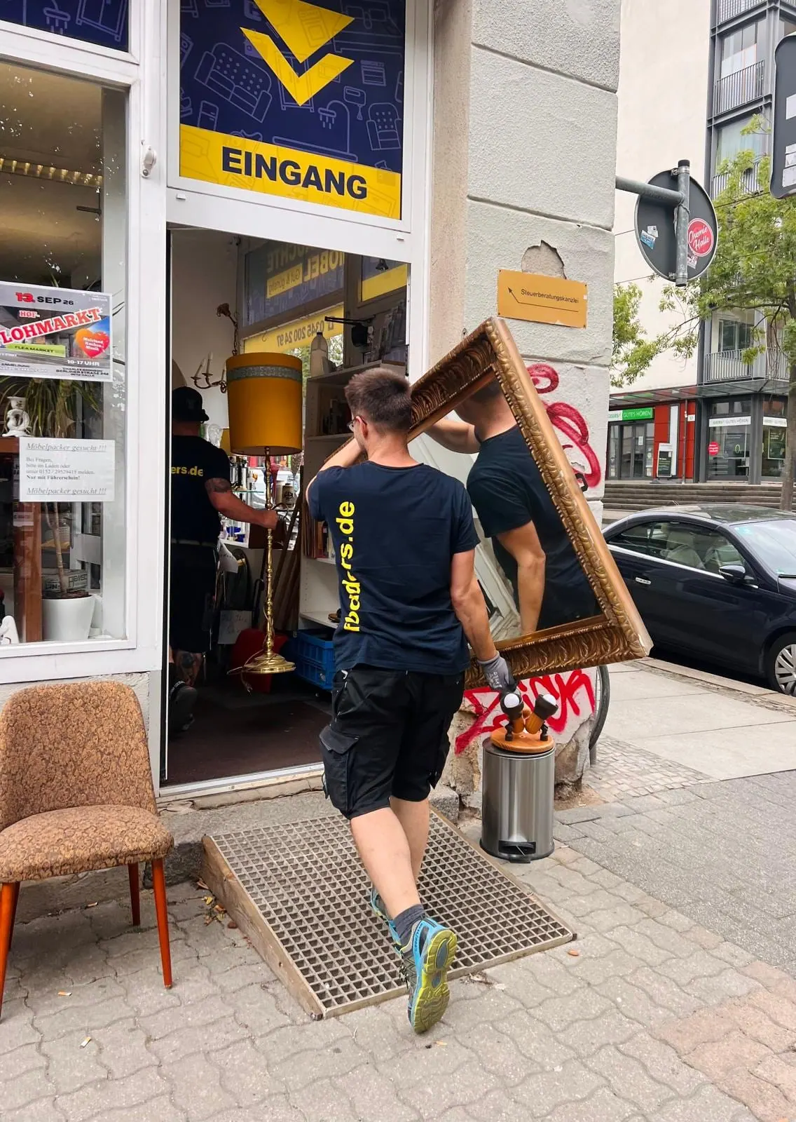 Zwei Mitarbeiter von Flodder's tragen einen großen Spiegel in das Ladengeschäft in Halle